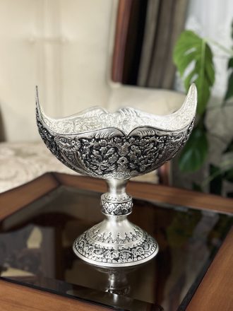 کشکول مسی سایز ۳ با نقش گل و مرغ ممتاز، اثری فاخر از هنر قلمزنی اصفهان است که با آبکاری نقره و تکنیک سیاه قلم، جلوه‌ای سلطنتی و هنری به فضای پذیرایی یا دکوراسیون شما می‌بخشد.